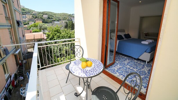 A balcony with a table, two chairs, and a view of a bedroom with a bed and a blue bedspread. - King Room with Balcony (Sorrento)