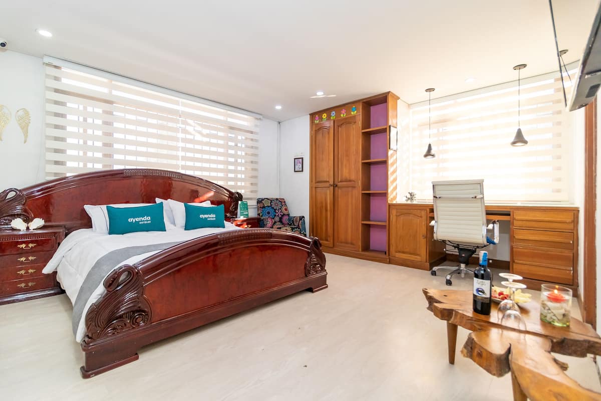 A bedroom with a wooden bed, a desk, and a chair. There is a wardrobe and a window with blinds.