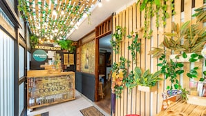Zona de recepción de hotel con mostrador de madera, cartel de recepción y pared verde con plantas.