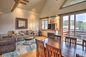 A spacious living room with a large wooden dining table, a sofa set, and a fireplace. - Mountain Views + Hot Tub: Big Sky Resort Condo! (Big Sky)
