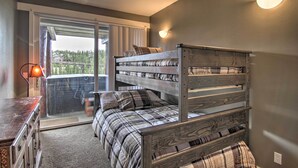 Ein Schlafzimmer mit Etagenbett, Kommode, Lampe und einer Schiebetür zu einem Balkon.