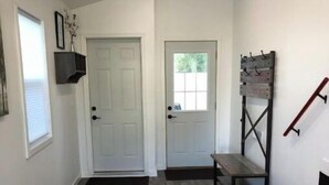 A hallway with a wooden floor, a white door, a bench, and a staircase.