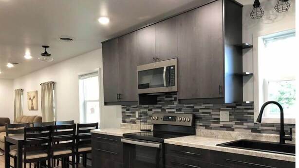 A modern kitchen with dark cabinetry, a microwave, stove, and a tiled backsplash.