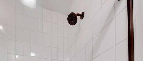 Un baño con azulejos blancos, ducha y una pequeña ventana con estante.