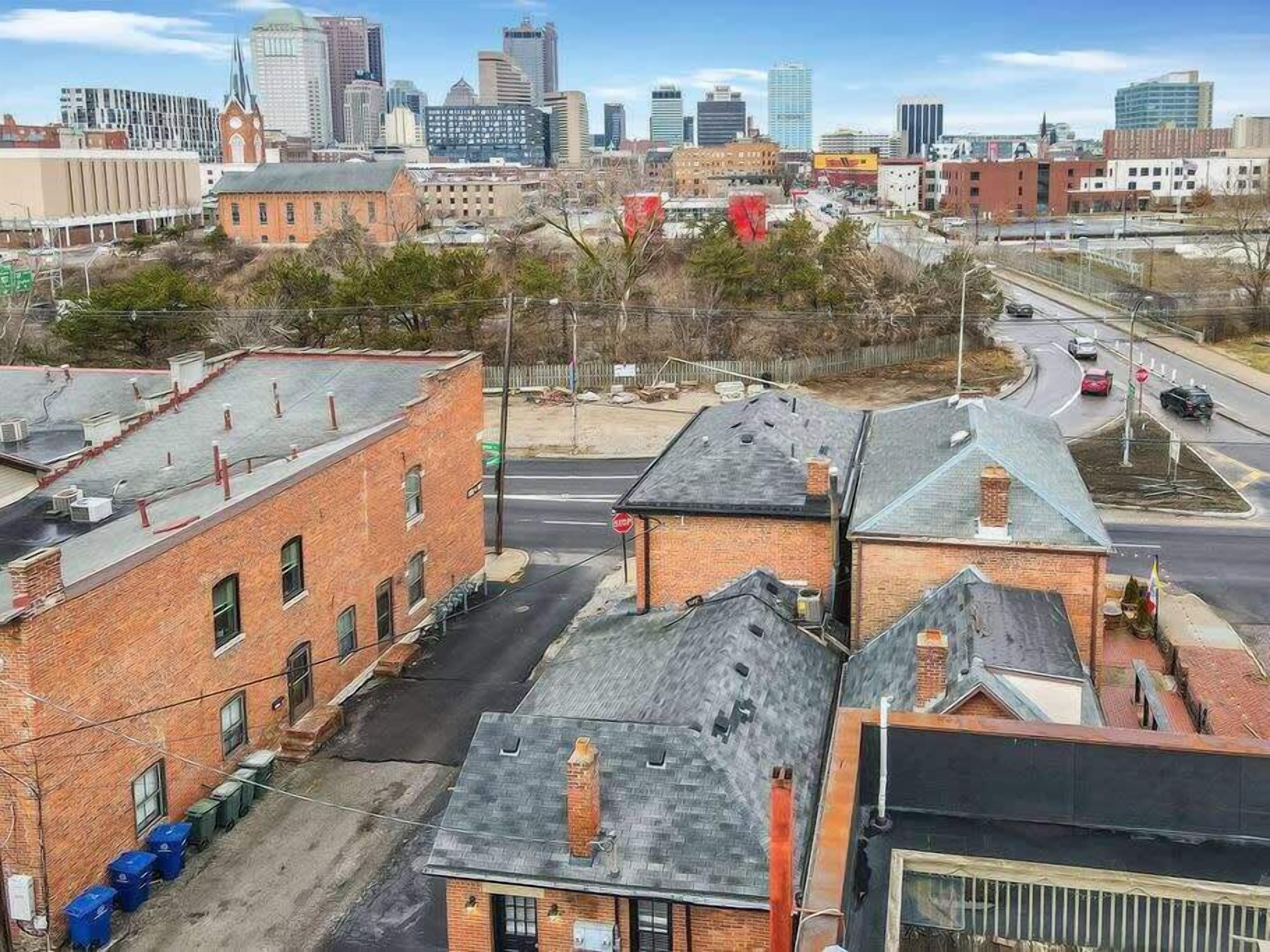 A cityscape with a mix of modern and older buildings, a clear sky, and a road with vehicles.