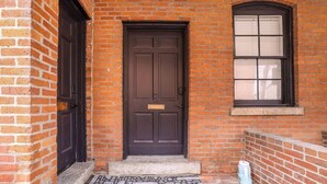 A brick building with a dark brown door and a window with blinds.