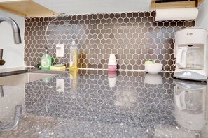 A kitchen with a hexagonal tile backsplash, a coffee maker, and a sink. - Minimalist Modern Suite Near German Village (Columbus)