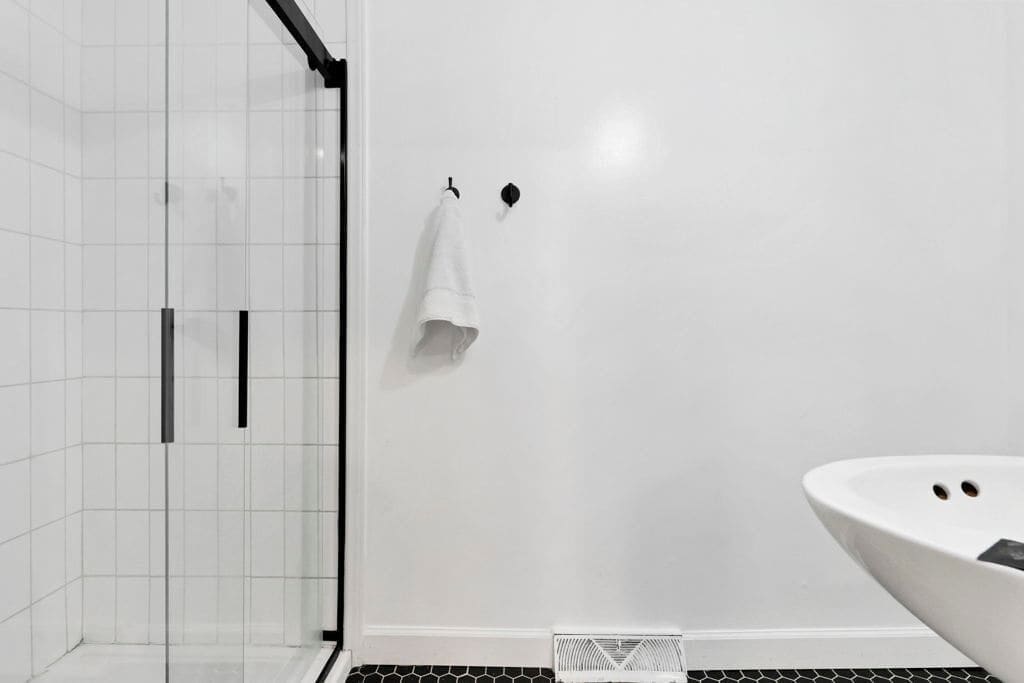 A bathroom with white tiled walls, a black shower door, a white bathtub, and a towel hanging on a hook.
