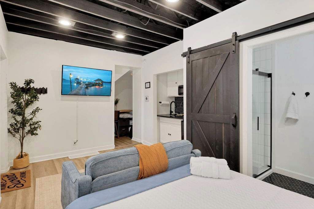 A modern hotel room with a bed, a sofa, a sliding door, a shower, and a view of a cityscape.