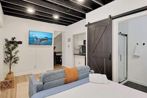 A modern hotel room with a bed, a sofa, a sliding door, a shower, and a view of a cityscape.