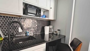 A compact kitchen with a black and white hexagonal backsplash, a microwave, a coffee maker, and a bar stool.