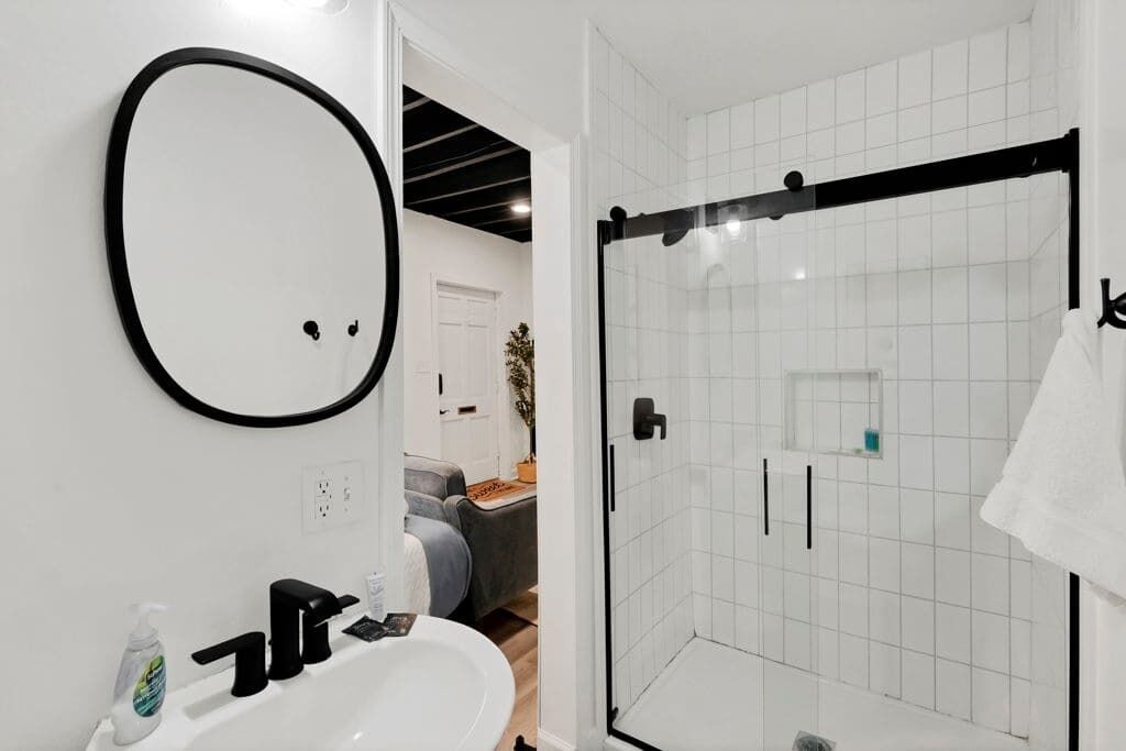Une salle de bain moderne avec une douche à parois de verre, un lavabo blanc et un miroir avec un cadre noir.