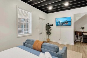 A modern living room with a sofa, a television mounted on the wall, a potted plant, and a desk with a chair.