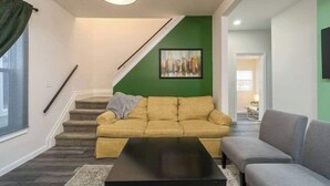 Un salon avec un escalier, un mur d’accent vert, un canapé, une table basse et un téléviseur.