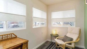 Une pièce avec de grandes fenêtres, une petite table, une chaise et un lampadaire.
