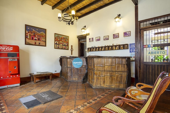 A lobby with a Coca-Cola vending machine, wooden furniture, a reception desk, and wall-mounted lights.