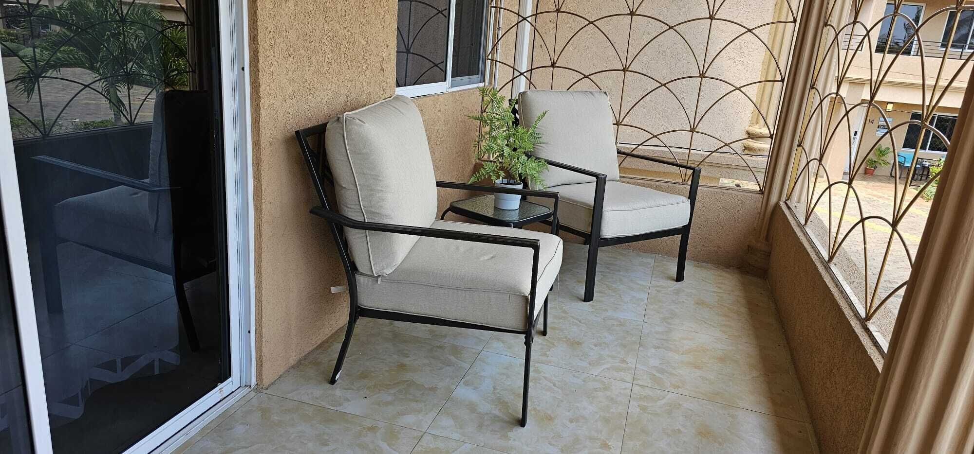 A balcony with two chairs and a small table, a potted plant, and a view of the street.