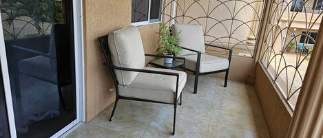 A balcony with two chairs and a small table, a potted plant, and a view of the street.