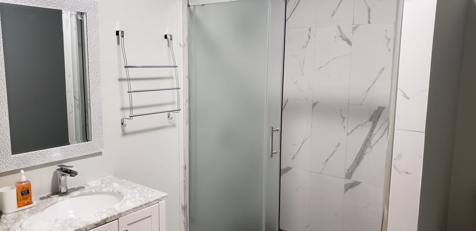 A bathroom with a marble sink, a mirror, a towel rack, and a glass shower door.