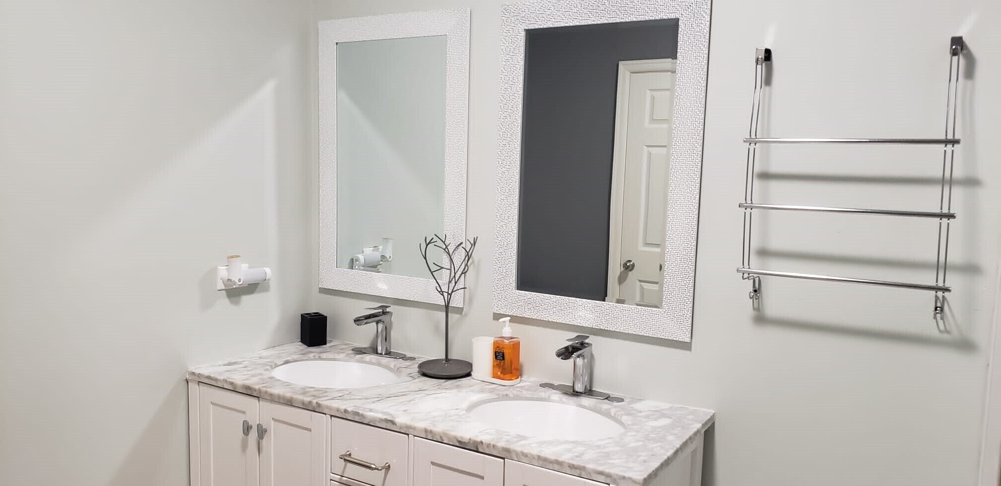 A bathroom with two sinks, a large mirror, a towel rack, and a soap dispenser.