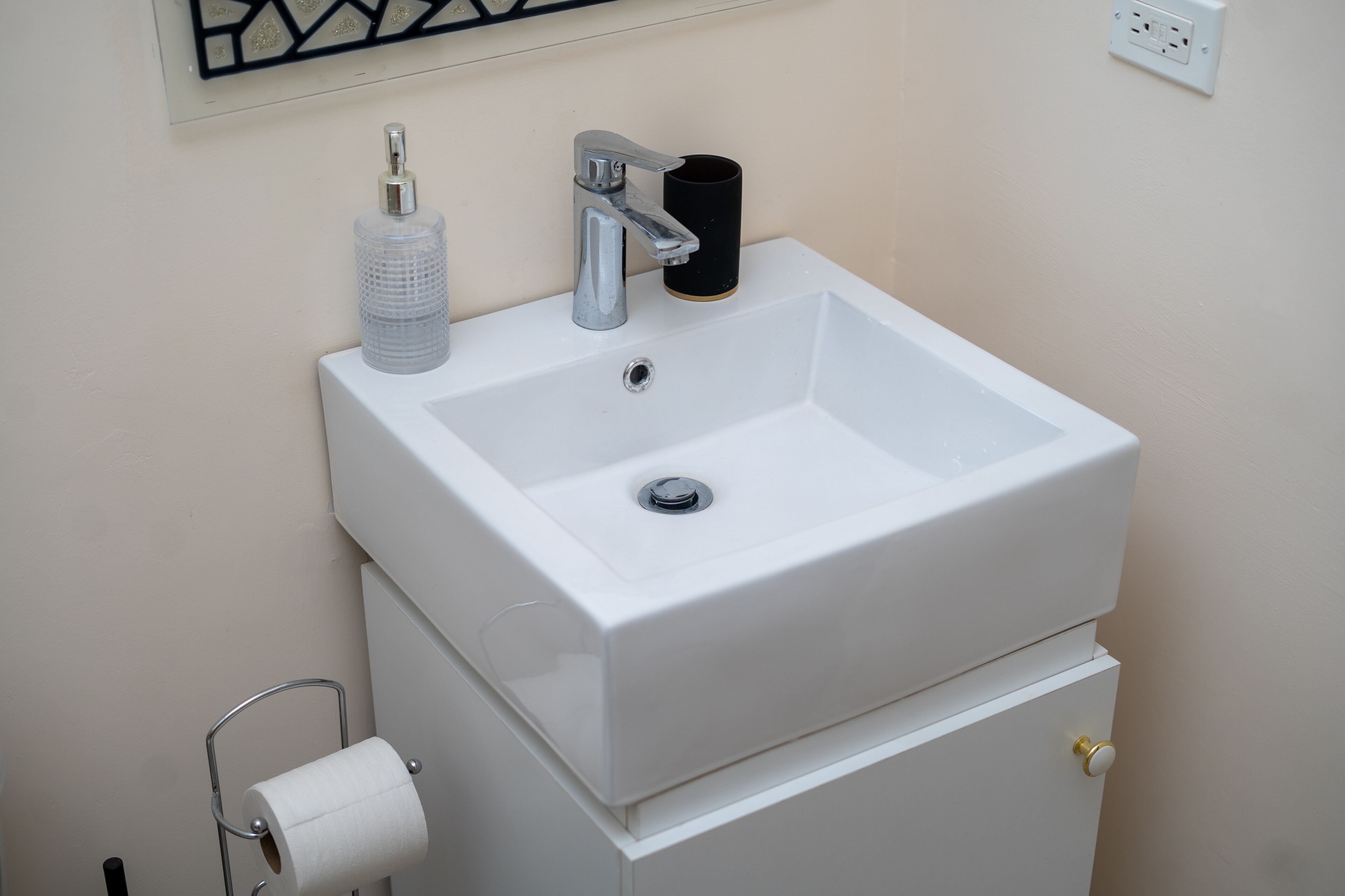 Un lavabo blanc pour la salle de bain, avec un robinet, un distributeur de savon et un porte-rouleau de papier toilette.