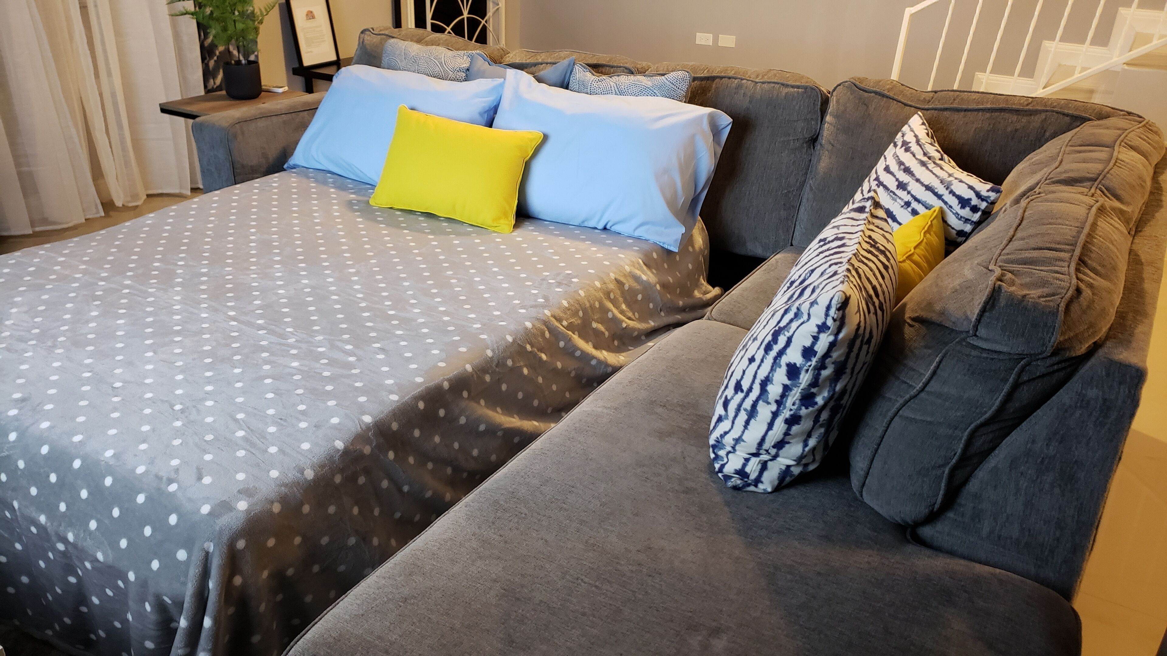 Un salon moderne avec un canapé gris, un plaid à motifs et un coussin jaune.