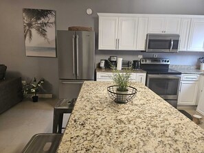 A modern kitchen with white cabinets, stainless steel appliances, a granite countertop, and a small potted plant. - Ubuntu De La Villa (Ocho Rios)