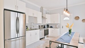 Une cuisine moderne avec des meubles blancs, des appareils en acier inoxydable et un coin repas agrémenté d’une nappe bleue.