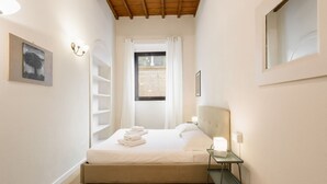 Une chambre à coucher comprenant un lit, une table de chevet, une fenêtre avec des rideaux, une étagère fixée au mur et un tableau.