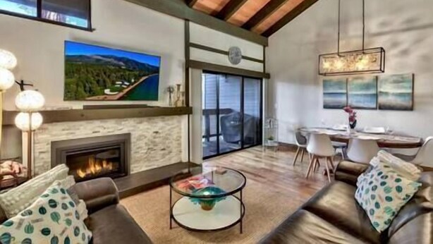 Una sala de estar moderna con chimenea, un televisor grande montado en la pared y un comedor con mesa y sillas.