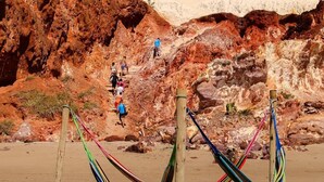A beach with colorful hammocks and people walking on a rocky path. - Pousada Cenário Ideal - Paradise is very close to you! (Icapuí)