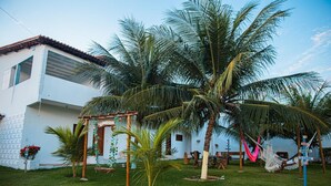 A white building with a tiled roof, surrounded by palm trees and a hammock. - Pousada Cenário Ideal - Paradise is very close to you! (Icapuí)