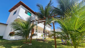 A building with a white facade and red-tiled roof, surrounded by palm trees and a well-maintained lawn. - Pousada Cenário Ideal - Paradise is very close to you! (Icapuí)