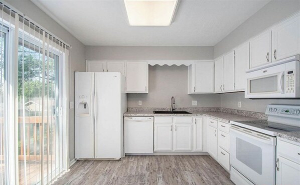 Una cocina con armarios blancos, un refrigerador, un microondas y un lavavajillas.