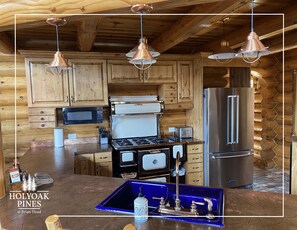Uma cozinha com armários de madeira, geladeira de aço inoxidável, fogão e luminárias pendentes.