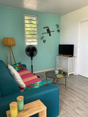 A teal-colored living room with a sofa, a TV on a stand, a fan, and a window with blinds.