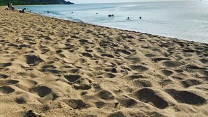 Una spiaggia sabbiosa con impronte, un mare calmo e uno sfondo collinare.