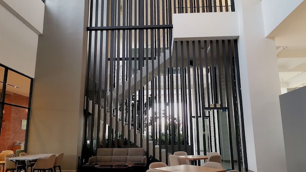 A modern interior with a high ceiling, a sectional sofa, and a dining area with tables and chairs. - Bell Suite Sepang KLIA Kota Warisan (Sepang)