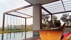 A modern outdoor pool area with a glass-enclosed structure, a wooden deck, and a large woven basket. - Bell Suite Sepang KLIA Kota Warisan (Sepang)