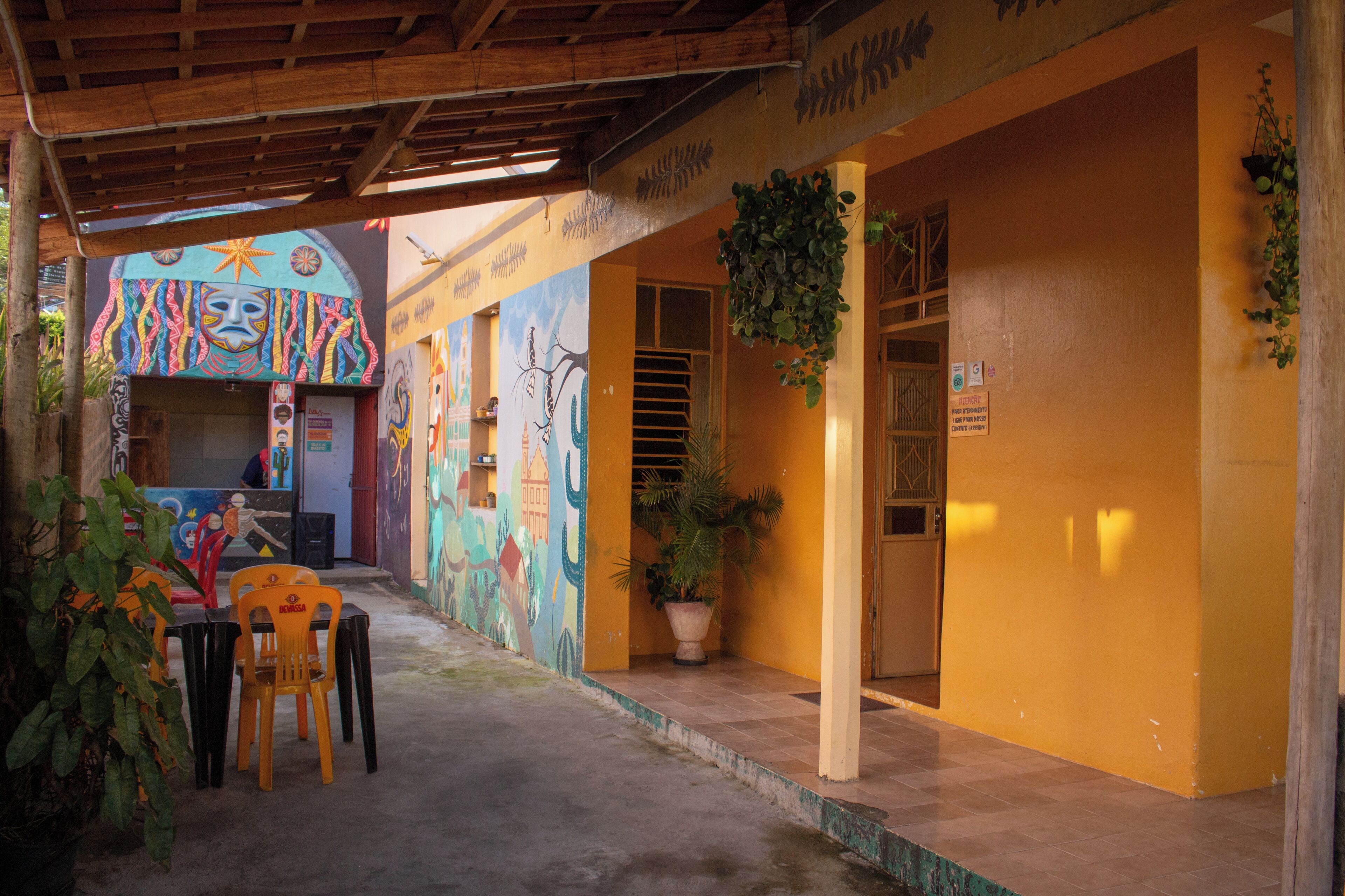 A covered outdoor area with a mural, a table with chairs, and a potted plant.