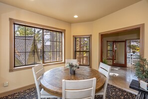 A dining area with a round wooden table, white chairs, and a vase with flowers.