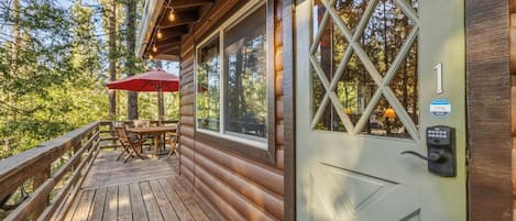 Une cabane en bois avec une terrasse, une table et des chaises, et un parasol rouge.