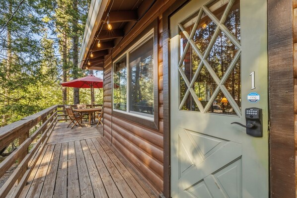 A wooden cabin with a deck, a table with chairs, and a red umbrella.