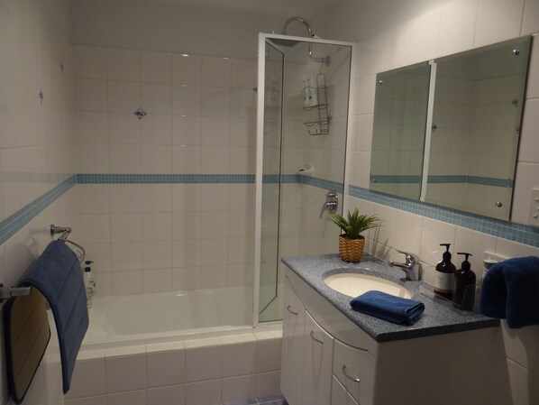 Un baño con cabina de ducha de vidrio, un lavabo con encimera de granito y un espejo sobre el lavabo.