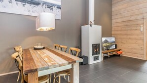 Un'area pranzo moderna con tavolo e sedie in legno, una lampada a sospensione, un caminetto e un'ampia finestra vista un paesaggio innevato.