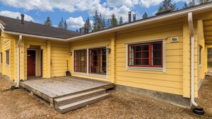 Un edificio giallo con una veranda in legno, una porta rossa e una finestra con cornice rossa.