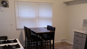 A compact kitchen with a dining table, four chairs, a stove, and a refrigerator.
