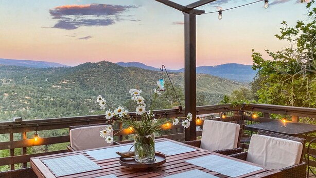 An outdoor dining area with a wooden table and chairs, a vase with flowers, and string lights. - Yosemite Lodge • Indoor pickleball, Basketball, Hot Tub, Game Room & EV (Oakhurst)