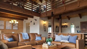 A spacious living area with leather sofas, a wooden coffee table, and a high ceiling with exposed beams. - Yosemite Lodge • Indoor pickleball, Basketball, Hot Tub, Game Room & EV (Oakhurst)