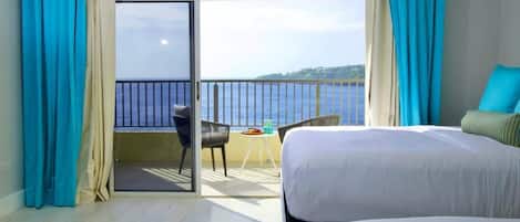 A hotel room with two beds, a balcony with a view of the sea, and a table with chairs.